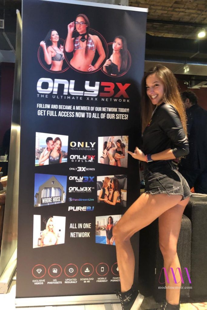 Amirah Adara posing beside Only3X promotional banner