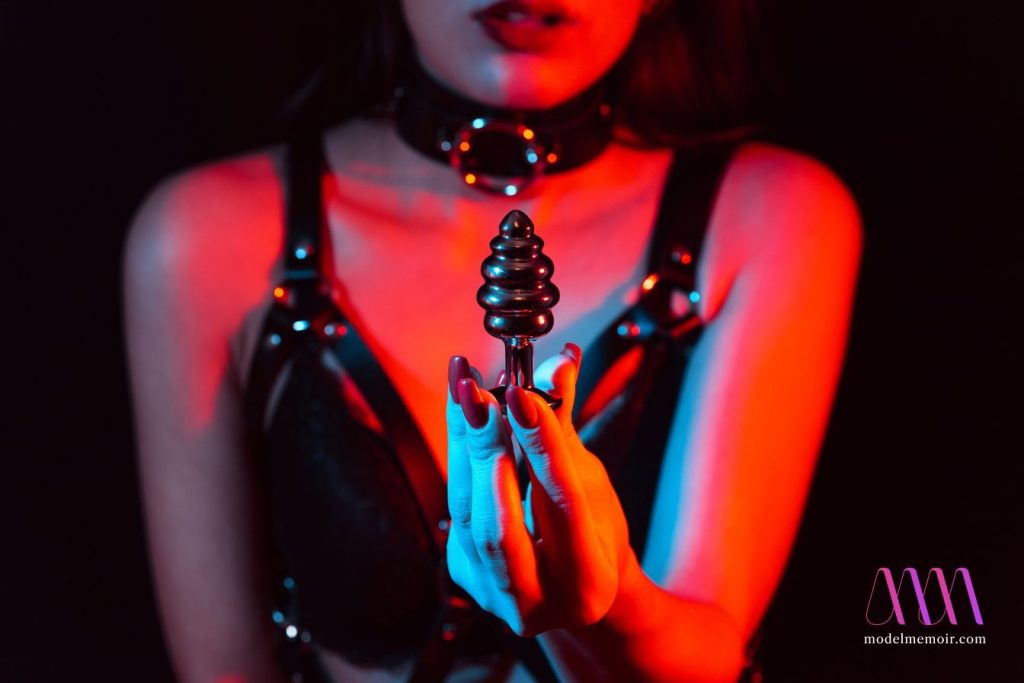 Metal butt plug in the hands of a girl with a choker.