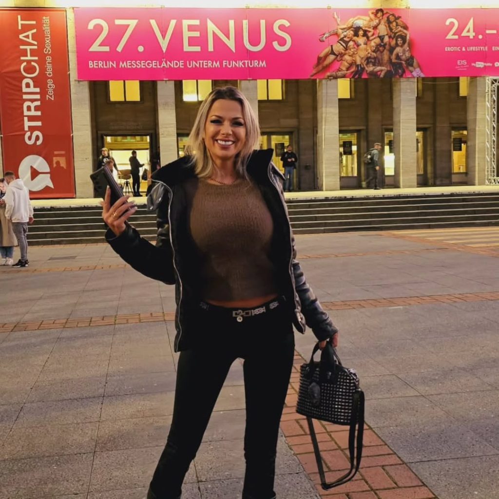 Shalina Devine smiling outdoors, standing in front of a Venus event sign.