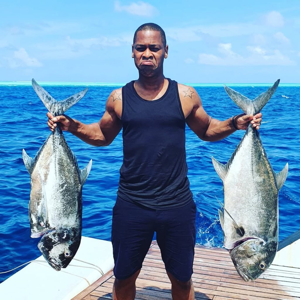 Darrel Deeps holding two large fish proudly, standing near the ocean.