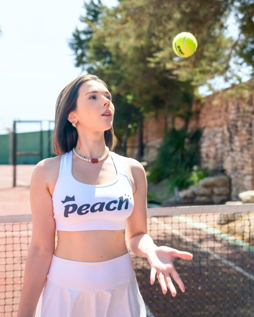 Eve Sweet in a sporty outfit, holding a tennis racket outdoors.