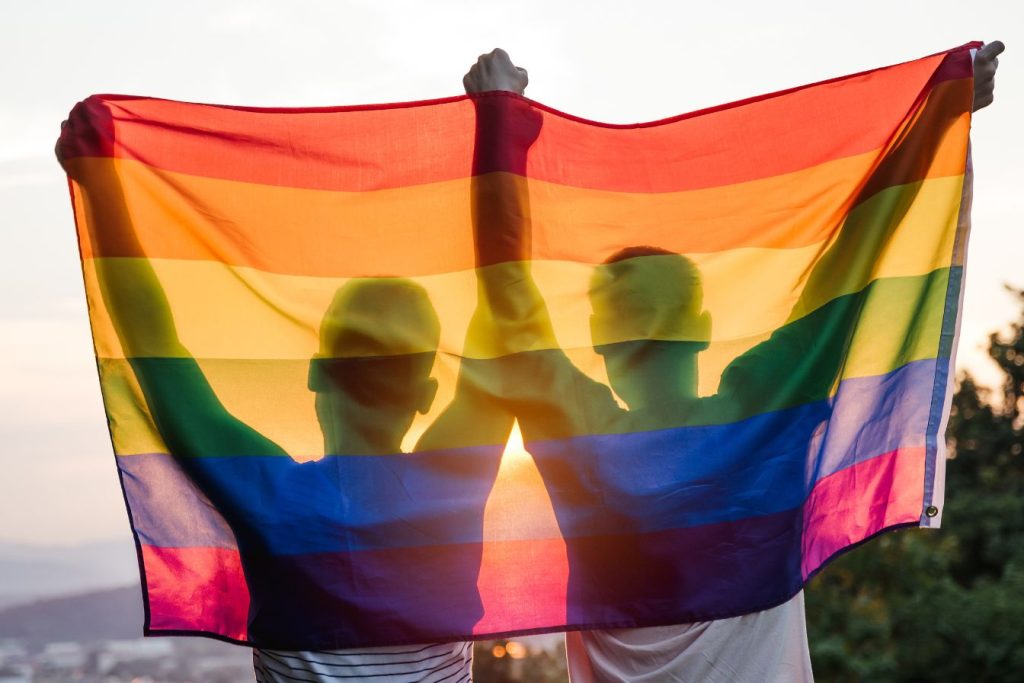 A gay couple holding an LGBTQ flag.