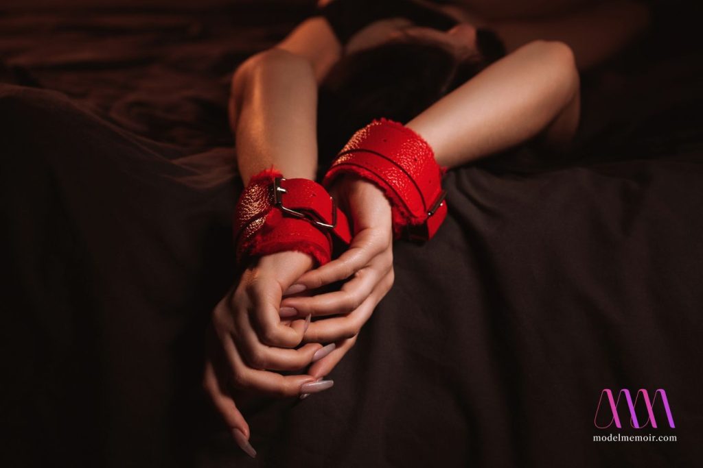 Female hands in red leather BDSM handcuffs.