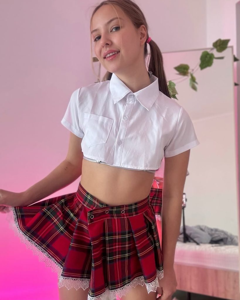 Tiny Angel posing in a schoolgirl outfit with a plaid skirt and white blouse.